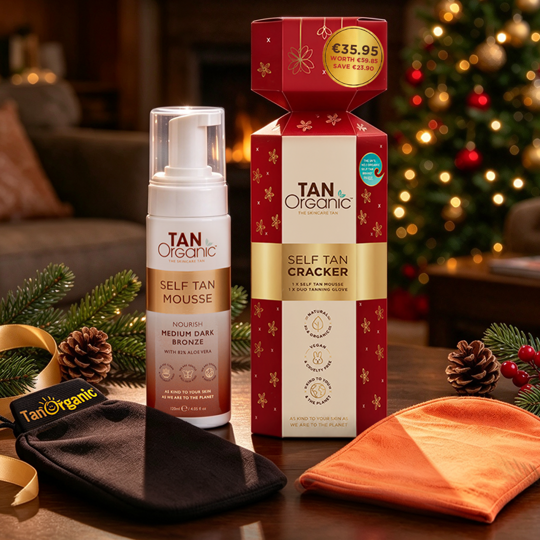 TanOrganic Self Tan Mousse Cracker gift set with mousse bottle and tanning gloves beside a Christmas tree.