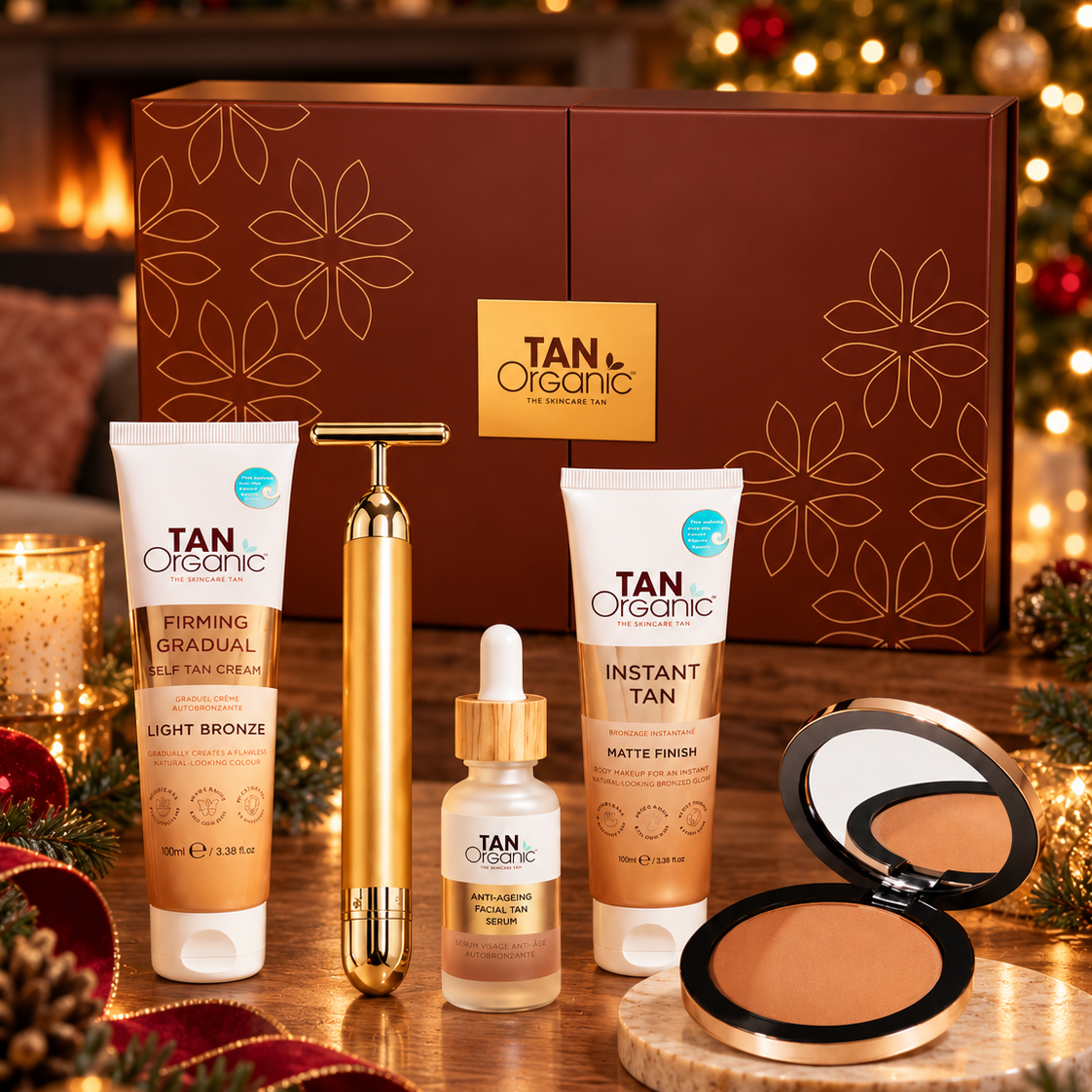TanOrganic Star Gift set with Firming Gradual Self Tan Cream, Instant Tan, Facial Tan Serum, bronzer and gold facial tool beside a decorated Christmas tree.